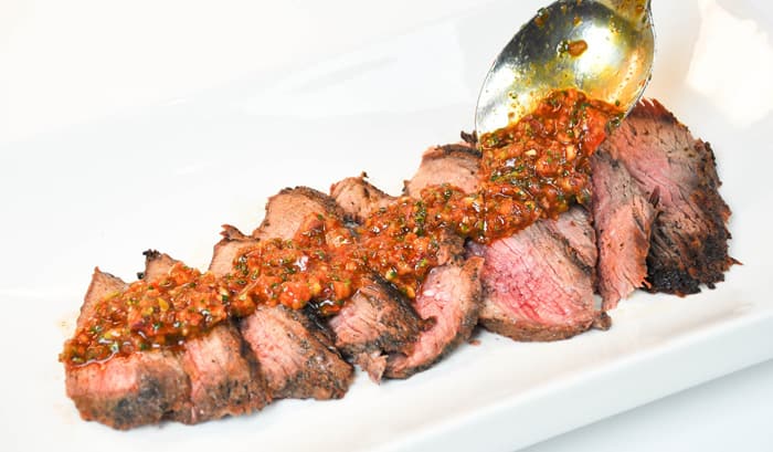 Chimichurri Rojo being poured onto the meat by a spoon.