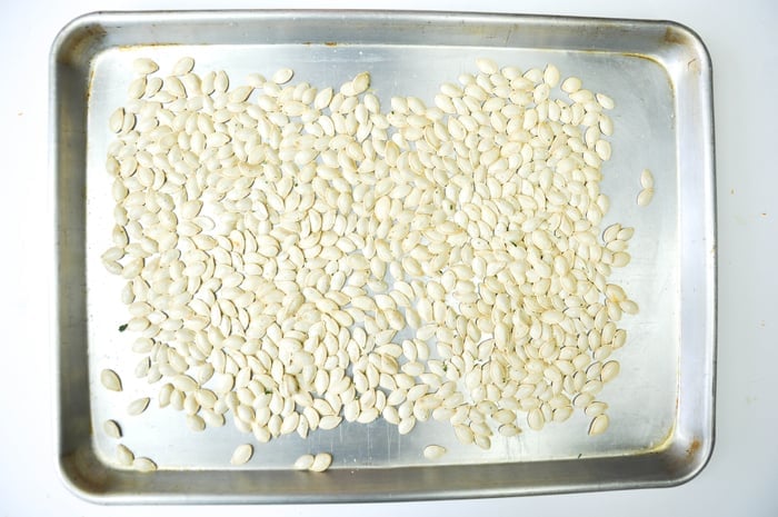 Pumpkin seeds with garlic salt on baking sheet.