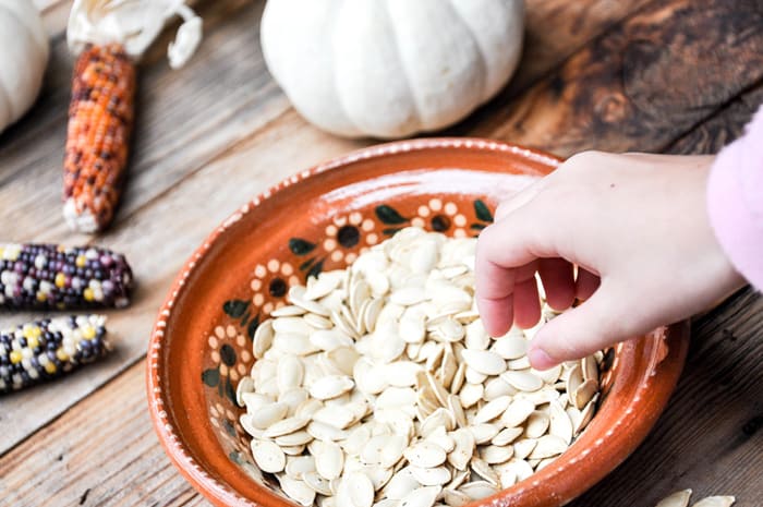 Hand reaching for cooked pumpkin seeds in bowl.