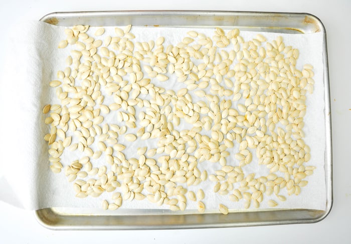Pumpkin seeds drying on paper towel on baking sheet